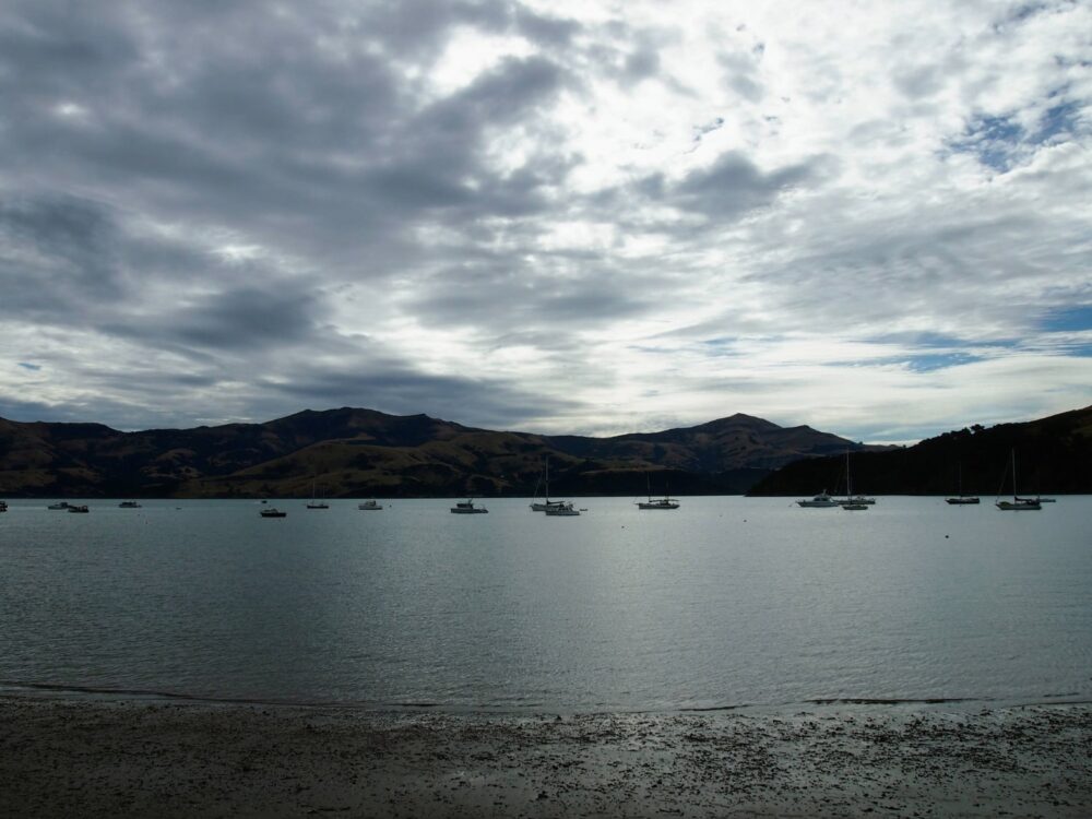 A moody photo of Akaroa harbour under cloudy skies, with several boats moored offshore