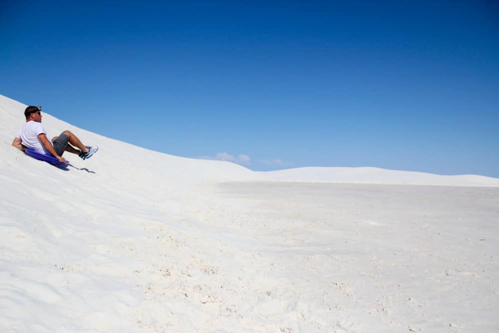 Man sliding down a white sand dune