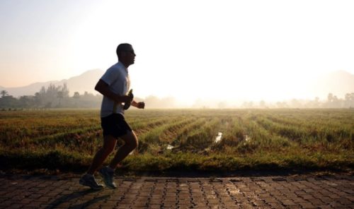 Man running at sunrise, silhouetted against a hazy backdrop with rice paddies in the foreground and hills in the background