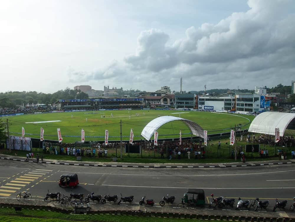 Cricket match being played at a ground in Galle, with a road visible in front