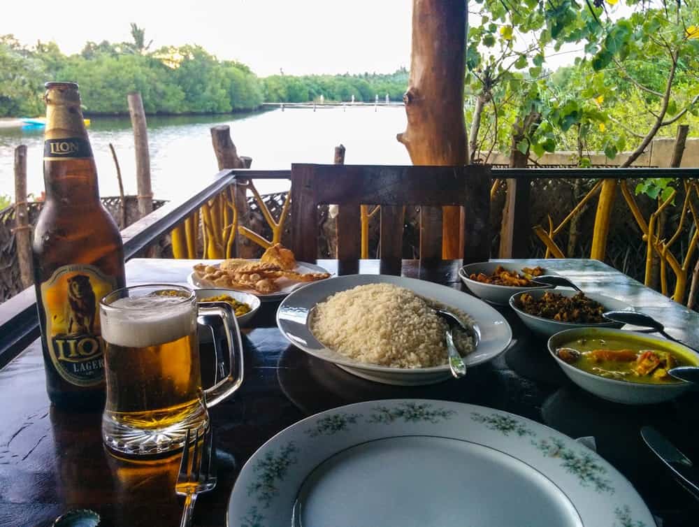 Rice and curry with bottle of beer on an outdoor terrace overlooking the water on Lonely Beach