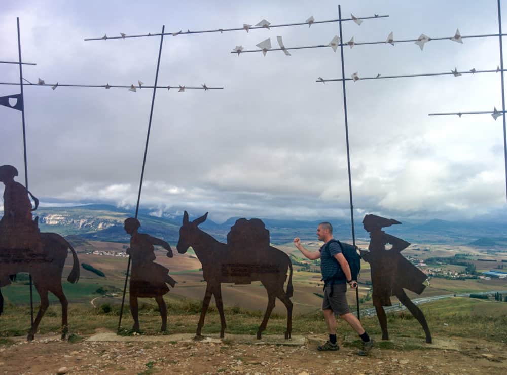 Author walking beside metal sculptures on a hilltop in Spain.