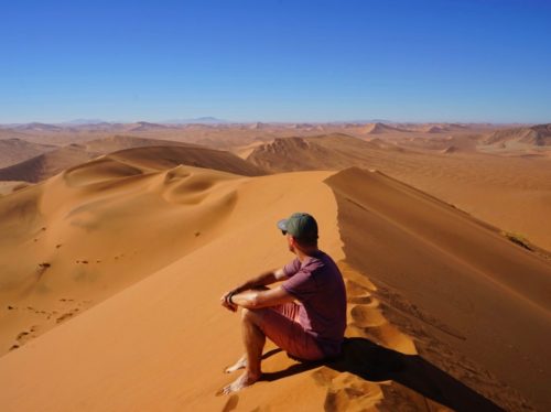Man sitting on sand dune looking out over a desert