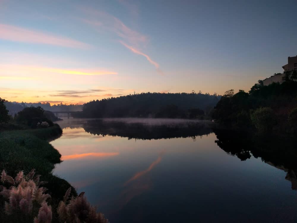 Sunrise over a lake, with mist on the water and a bridge visible in the distance.