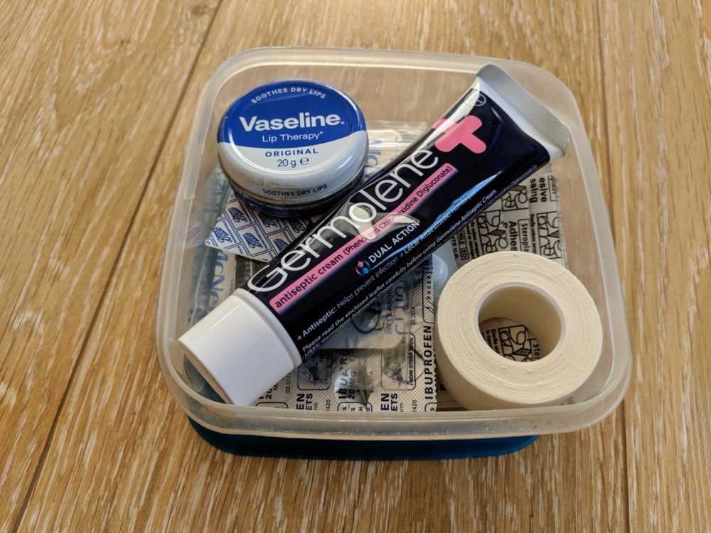 Small first aid kit with painkillers, vaseline, antiseptic cream, and bandaids, on a wooden floor.