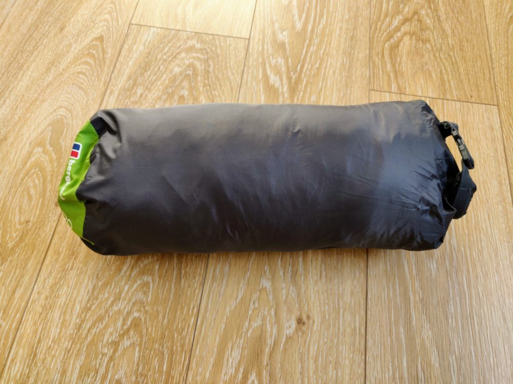 Sleeping bag (rolled up in a bag) on a wooden floor.