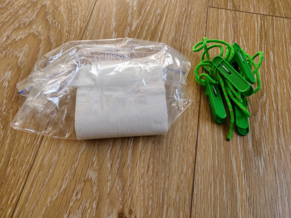 Toilet paper in a plastic bag with a bundle of pegs and washing line alongside, on a wooden floor.