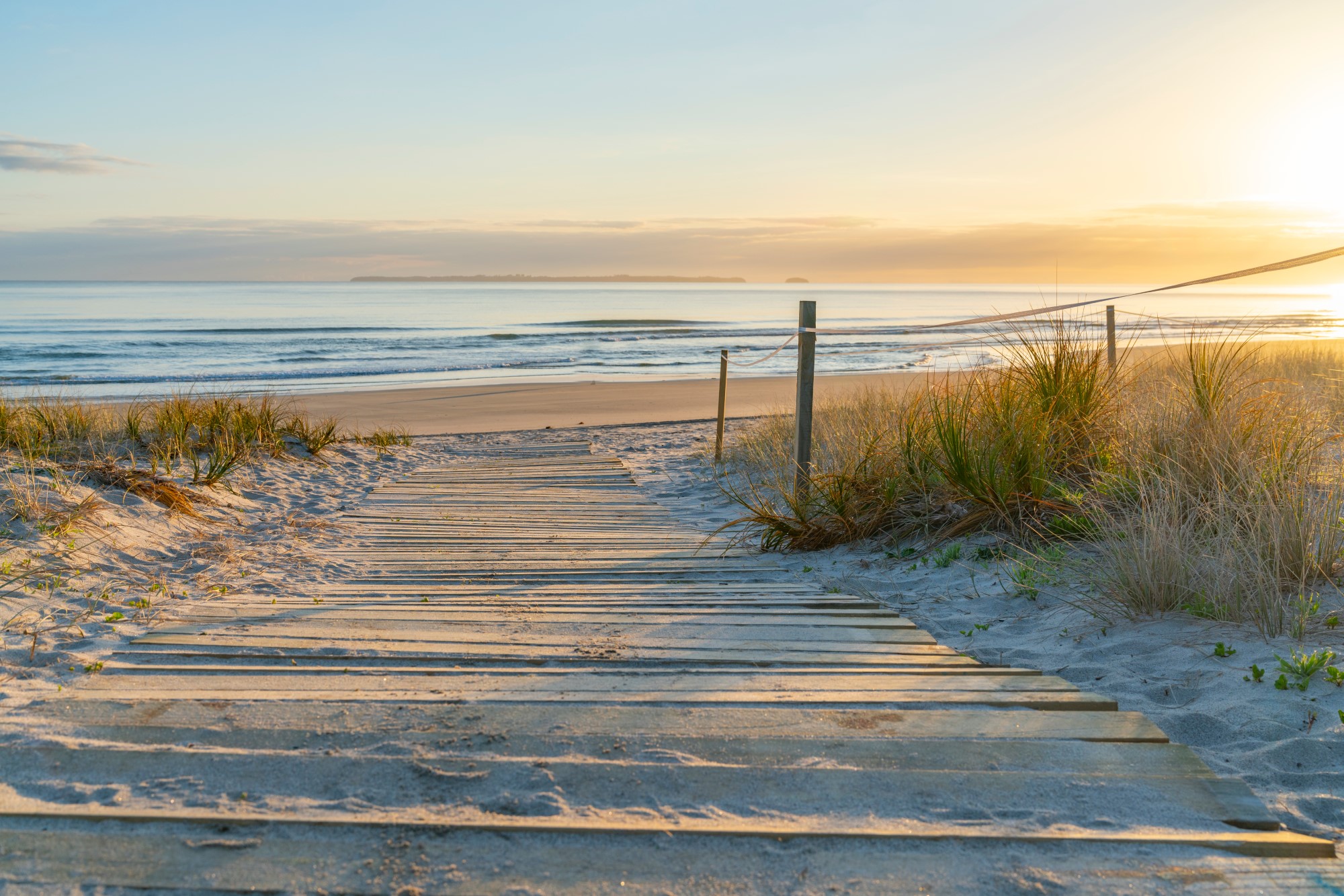 View over a walkway onto Papamoa Beach at sunset