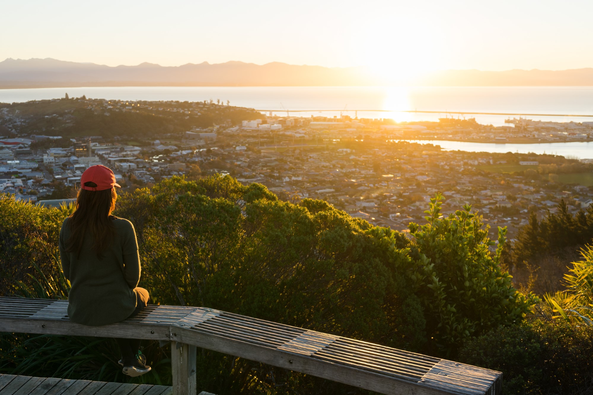 Woman looking out at the view from the top of the Centre of New Zealand walk at sunset in Nelson, New Zealand