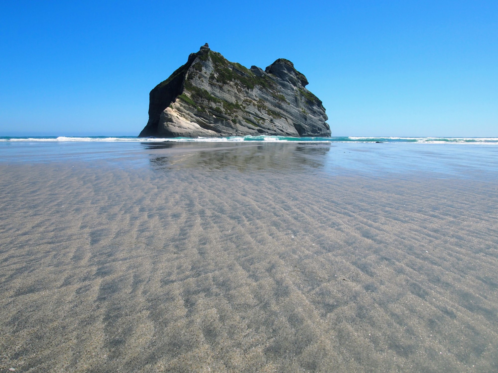 Rock and reflections in the sand at low tide at Wharariki beach, Golden Bay, New Zealand
