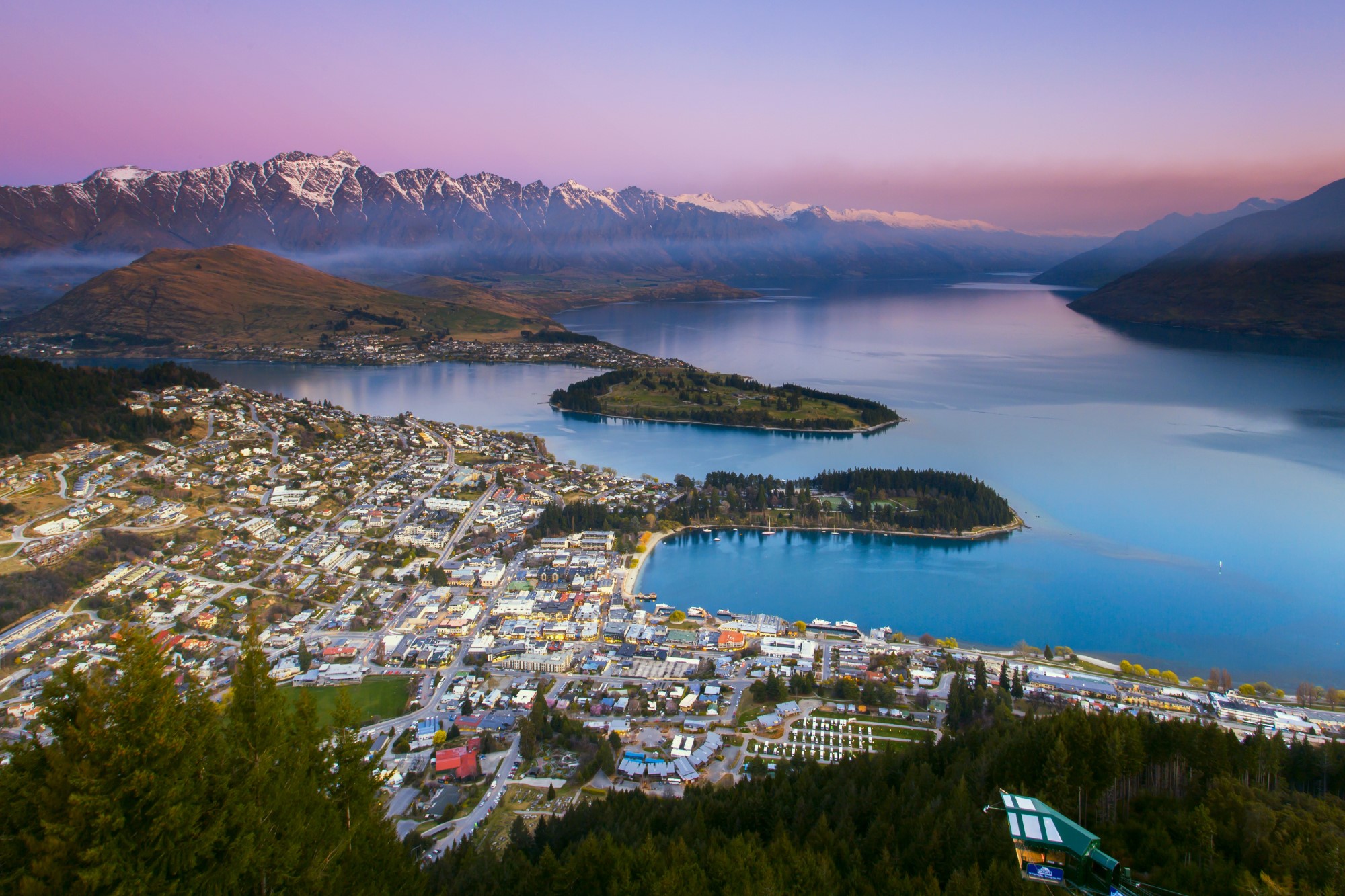 View over lake, mountains, and the town of Queenstown, New Zealand, at sunsetth