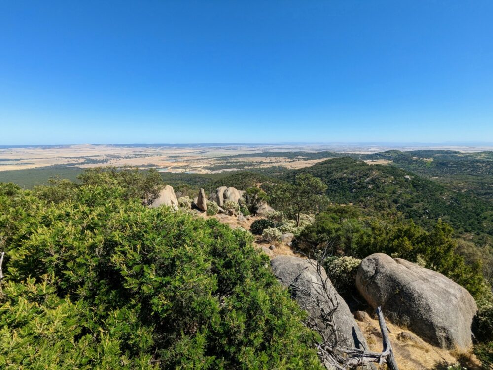 View from the top of Flinders Peak, You Yangs Regional Park, Victoria, Australia, looking over rocks and trees towards farmland and ocean in the distance