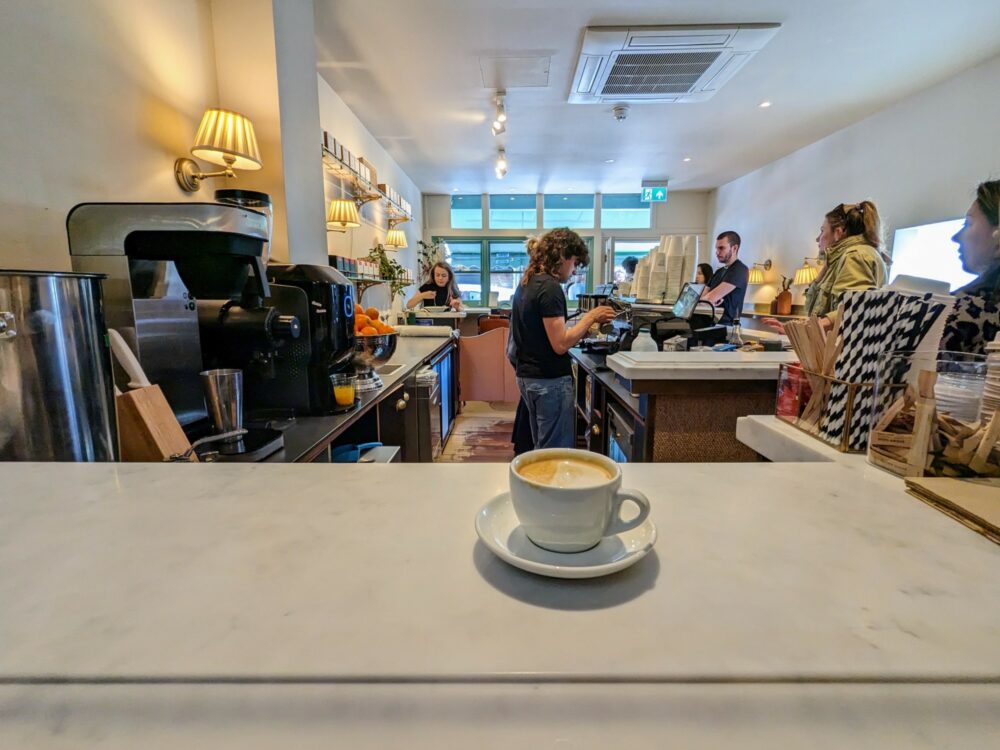 Interior view of Hagen Espresso, with coffee on counter in foreground, staff members making coffee behind, and several customers waiting for drinks