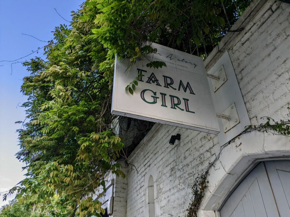 Sign for Farm Girl cafe on white brick exterior wall, with tree branch growing over the top left corner