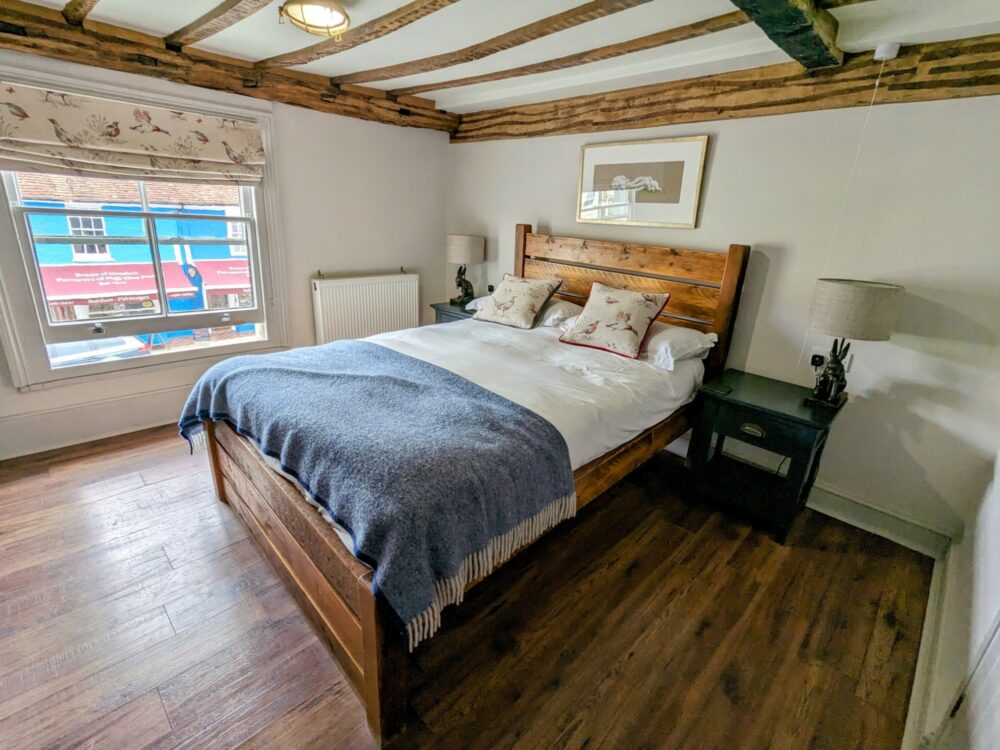 Bed in cozy room above a pub, with wooden floors and bed frame, exposed beams, and simple decorations.