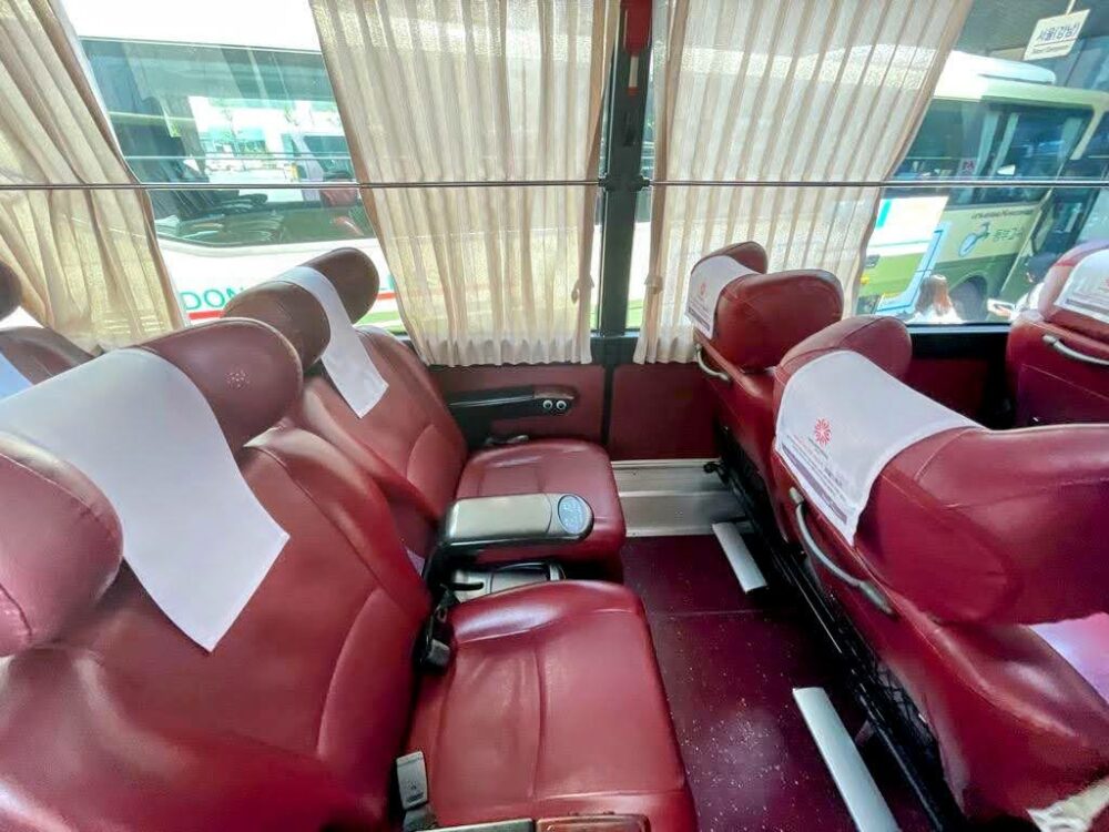 Luxurious-looking red leather seats with cushioned headrests, arranged in pairs on a bus in South Korea. Curtains on windows alongside.
