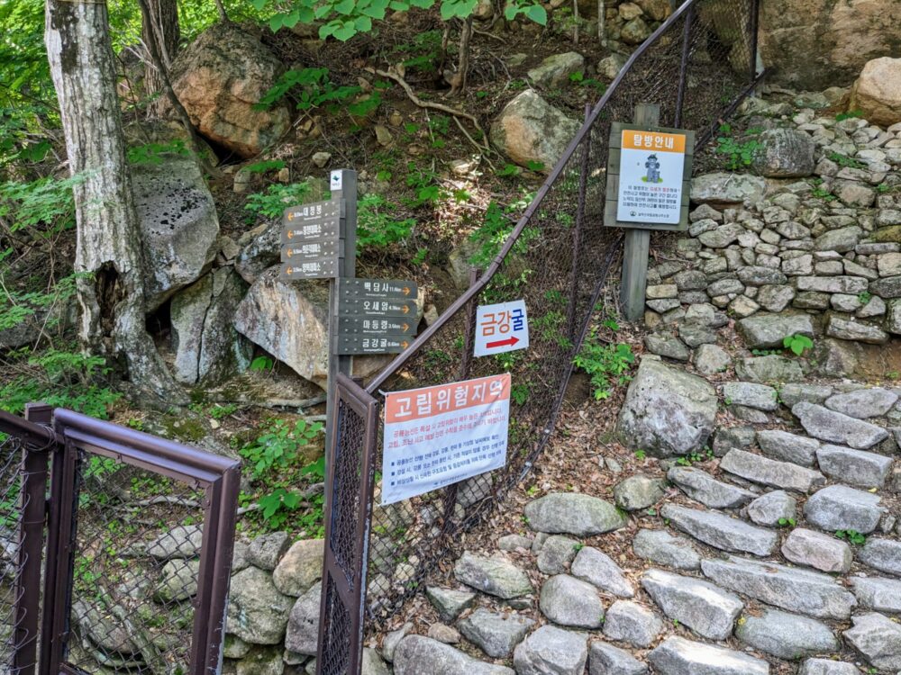 Signposts for several different hiking trails in Seoraksan National Park, four pointing to the left and five to the right. The right-hand path is steep stone steps, with a metal fence alongside.