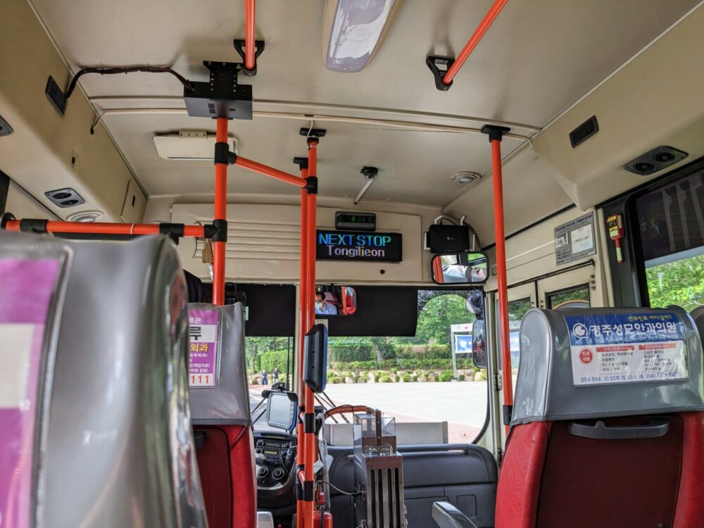 Inside of a bus in South Korea, taken from a seat near the front, with electronic signage that says "NEXT STOP: Tongiljeon" above the front window