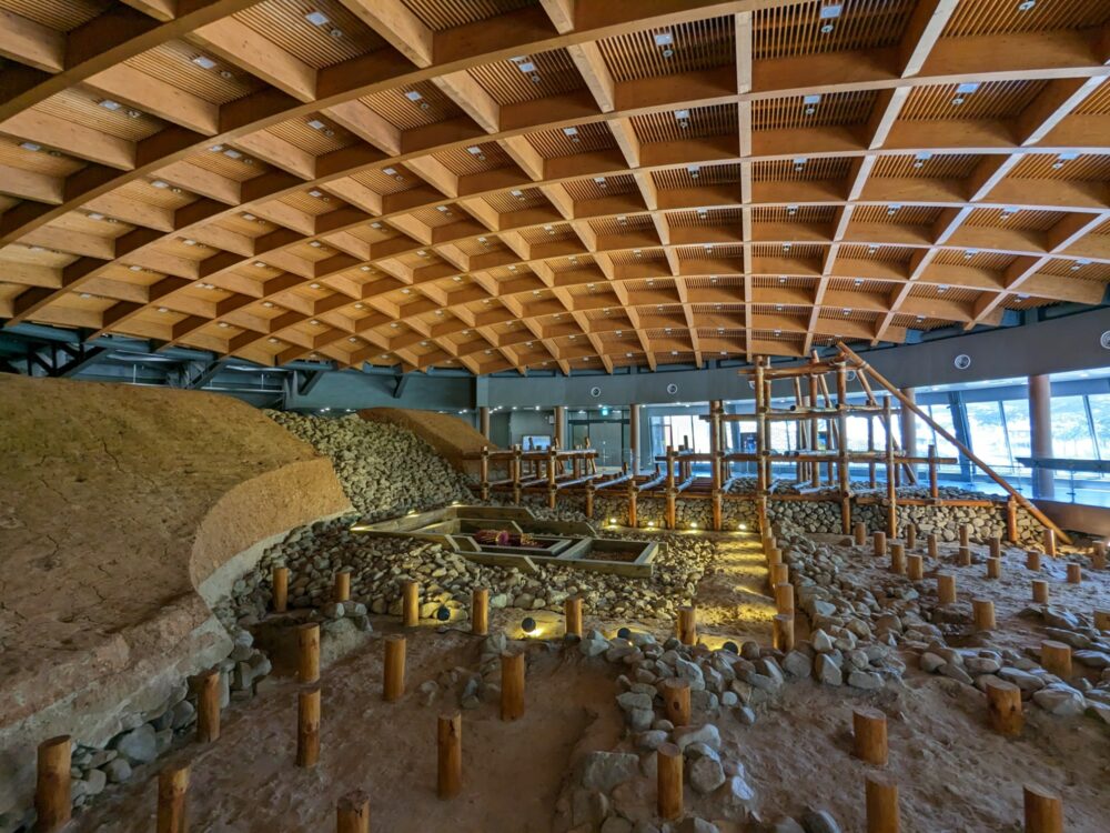 Inside the Geumgwanchong tomb museum in Gyeongju, with curved, criss-crossing wooden beams on the roof and a recreation of the construction process below. 