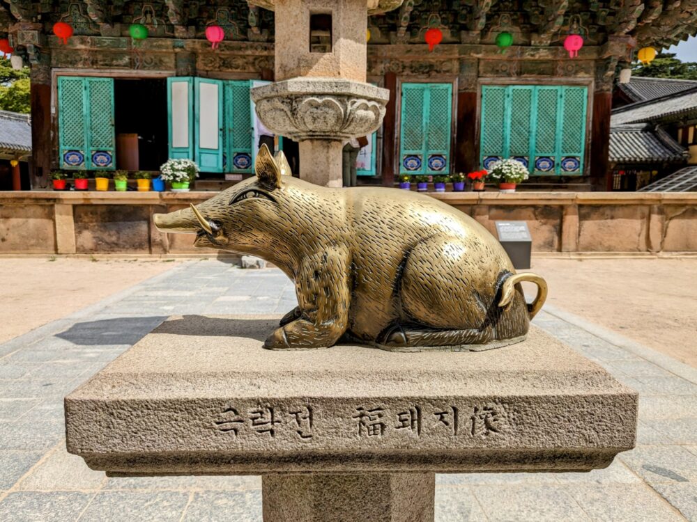 Closeup of a small statue of a golden pig, sitting on a stone pedestal in front of a temple building in Bulguksa, South Korea