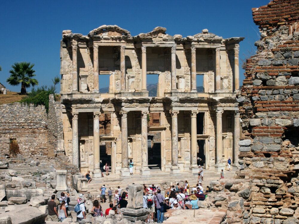 The ruins of the library of Celsus at Ephesus, the front facade of which has two storeys of marble columns and carvings. Many people are standing in front of it taking photos.