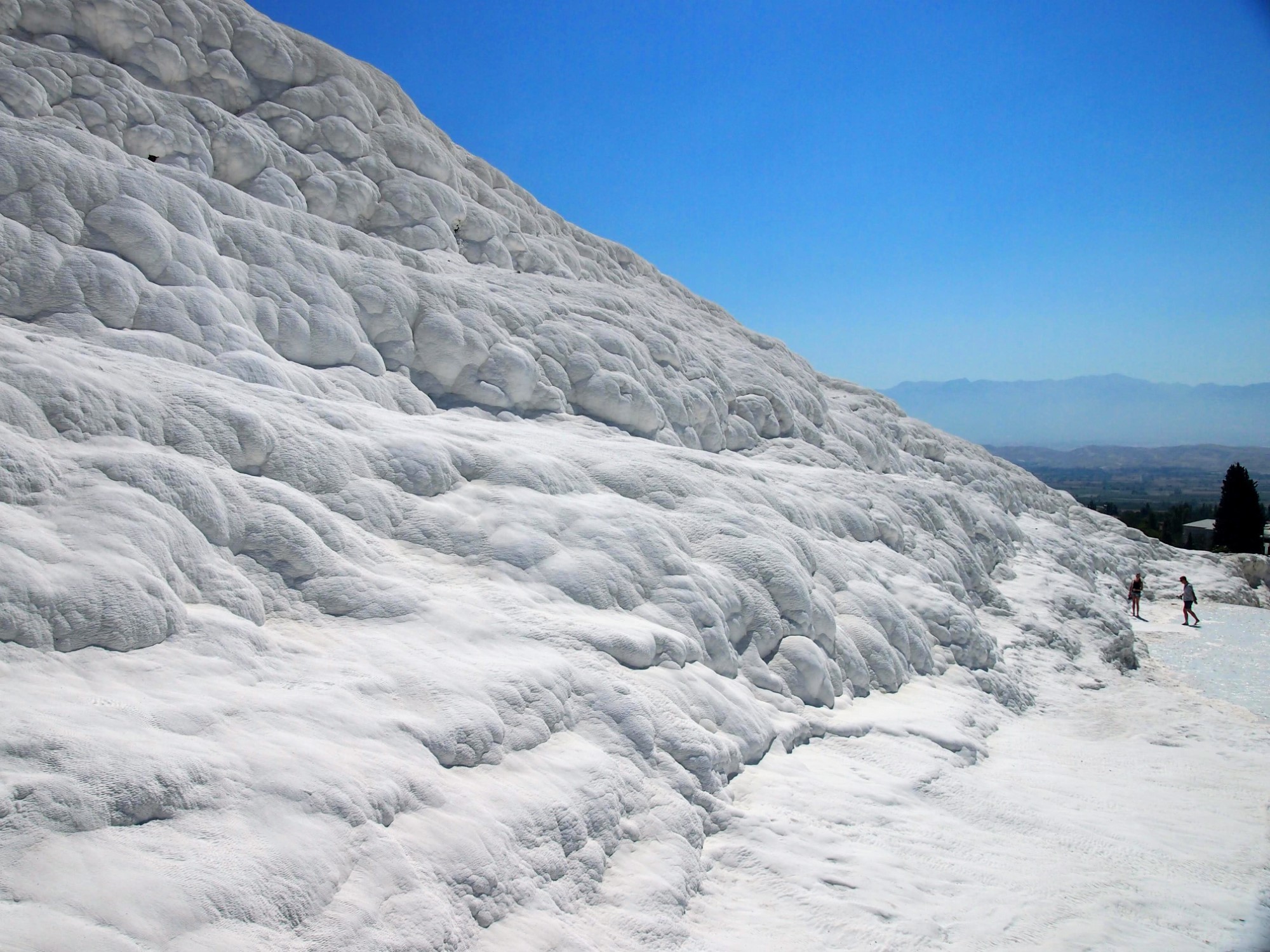 Large slope of snow-like white travertine at Pamukkale, with two people in the middle distance