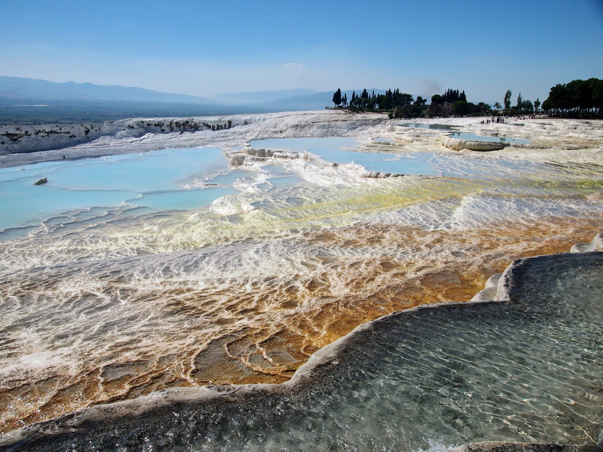 Wide overview of the travertine at Pamukkale with several different colors and pools. People visible in the distance