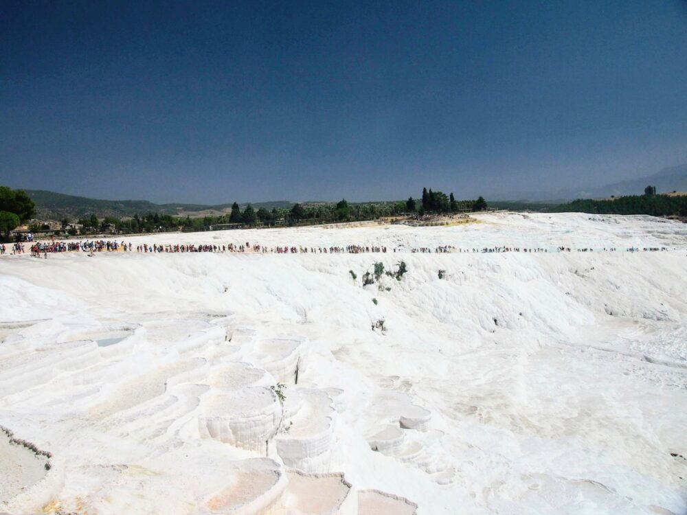 Wide overview of the travertine at Pamukkale with a long line of people visible in the middle distance