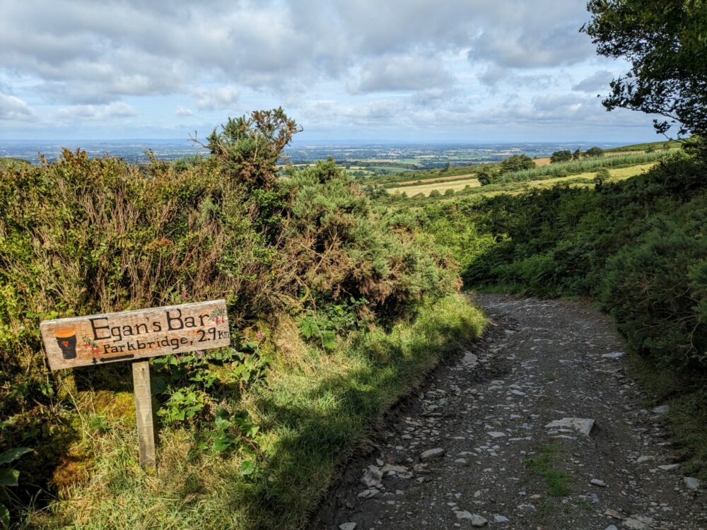 A wooden sign on the side of a stony path pointing towards Egan's Bar in Parkbridge, 2.9km away on the left.