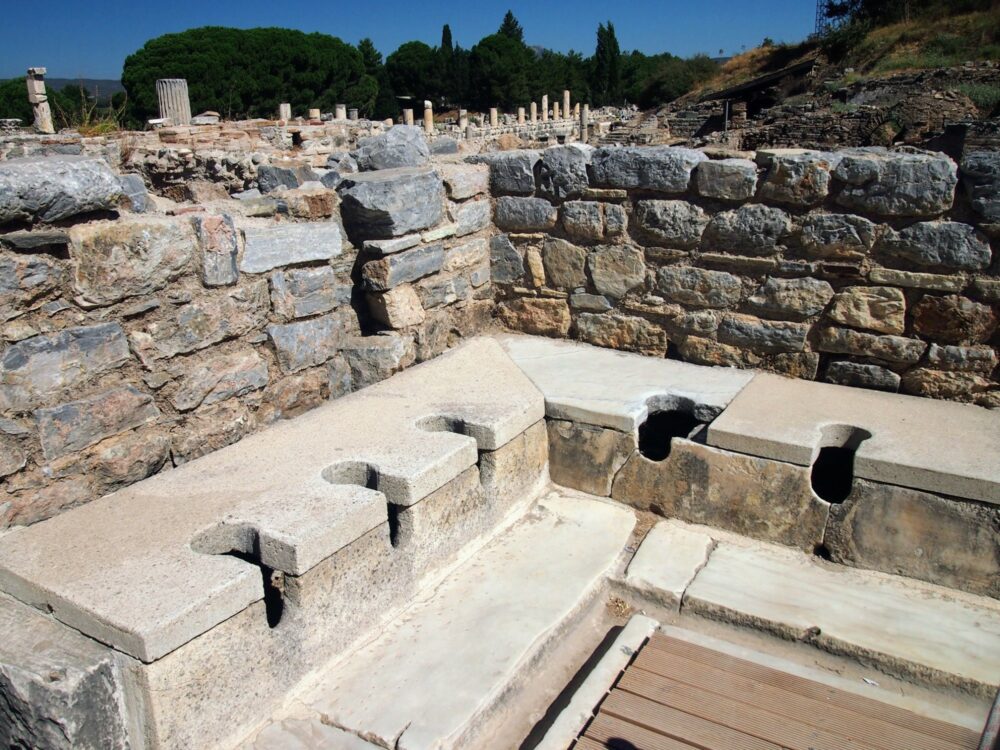 Ancient public toilets at Ephesus, with a stone sitting area that has holes cut into it.
