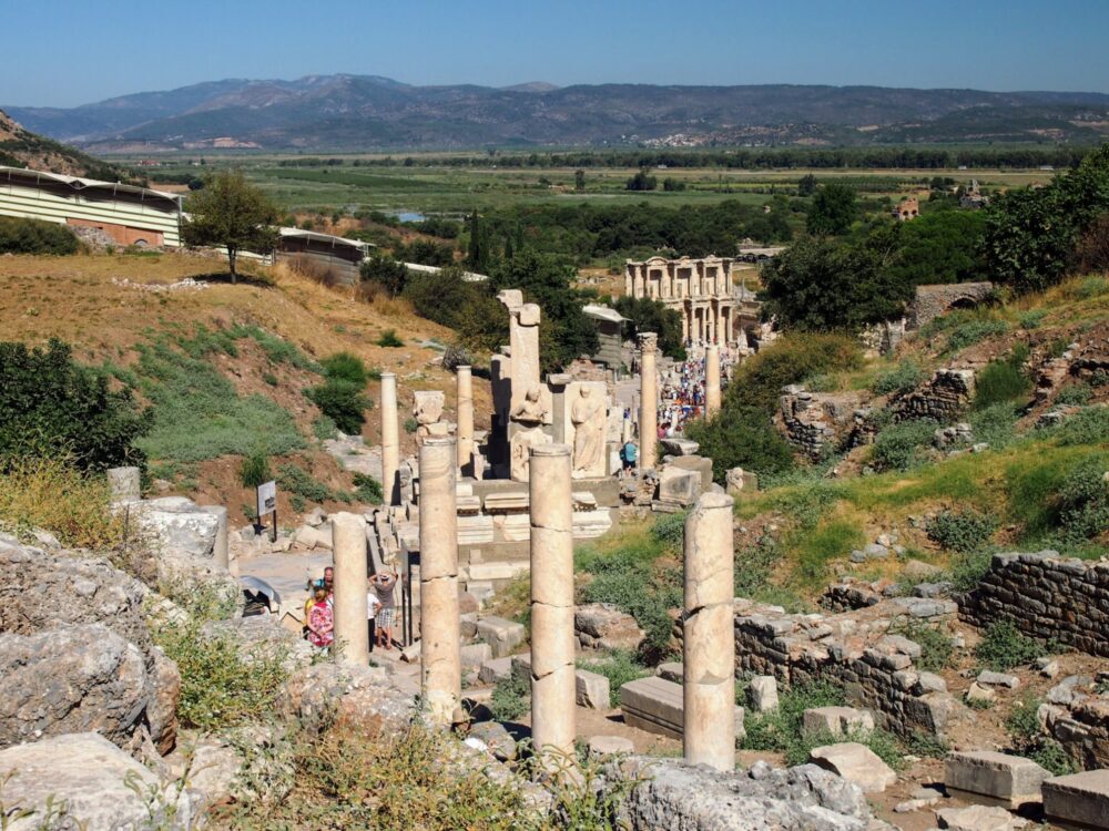 View towards the Library of Celsus in the middle distance, with a path flanked with columns leading to it and countryside behind.