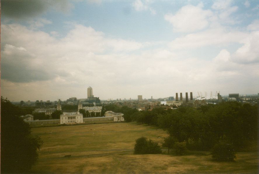 Grainy photo from the late 1990s of a view from a hill of an expansive park on a cloudy day, a grand historic building, with a single tall building visible in the background.