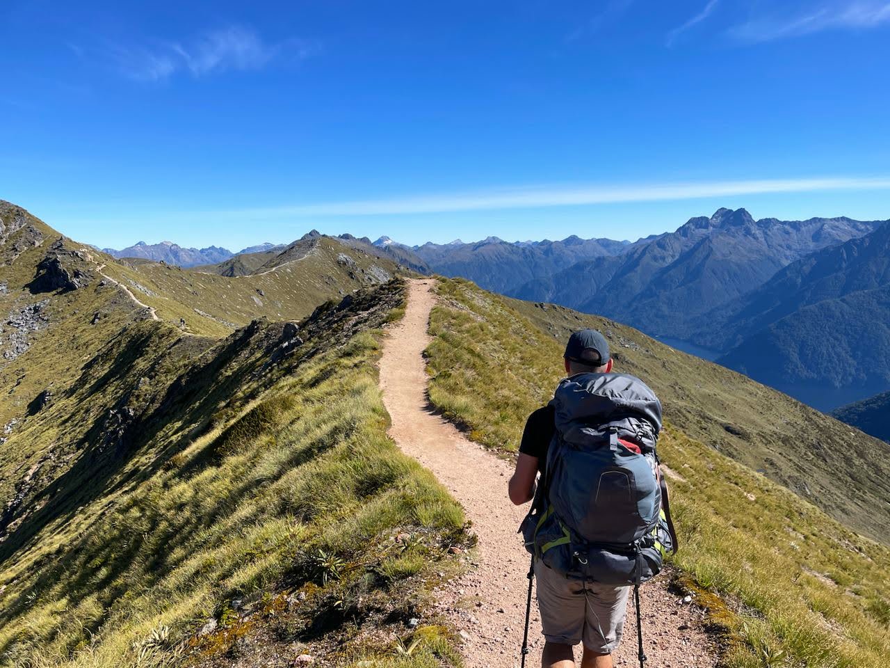 Man walking with a backpack on a narrow path along a ridgeline