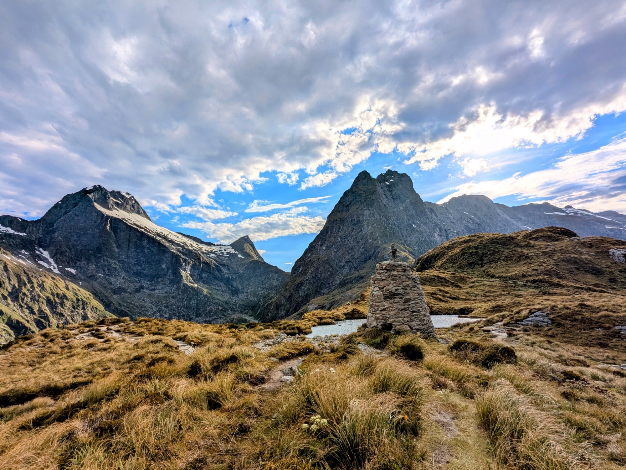 Looking towards a stone memorial with a lake beyond and tall mountains in the distance