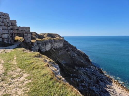 View along low cliffs with a rocky beach beach below. Large stone blocks have been arranged into an archway above a walking path.