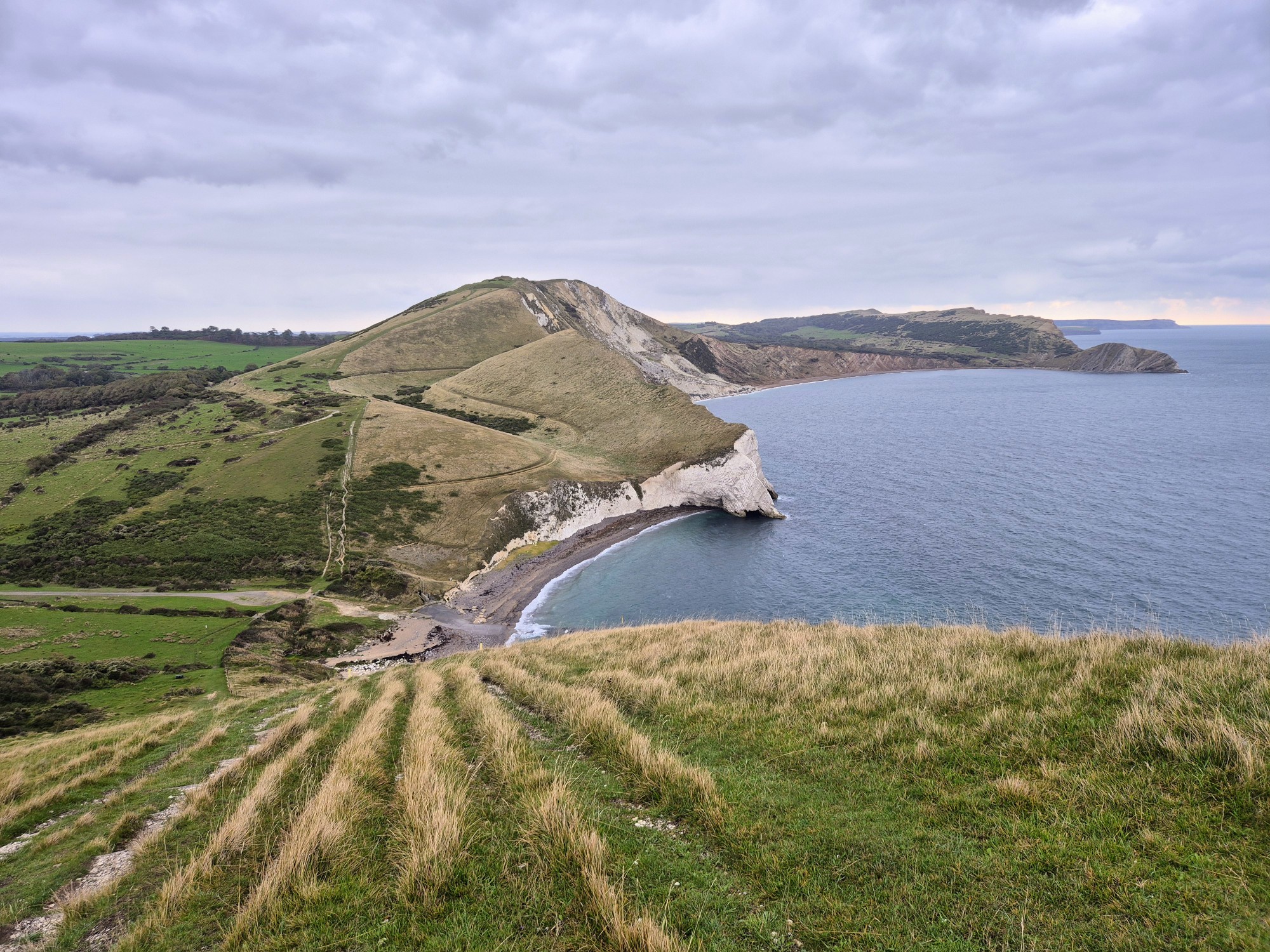 Steep grass and stone path leading down towards a small cove. The path continues back up steep cliffs on the other side.